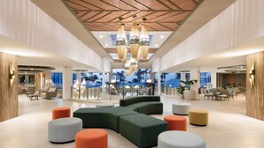 A spacious lobby with a modern design, featuring a large seating area with colorful ottomans, a central green sofa, and a ceiling with hanging pendant lights. - Hotel Riu Paraiso Lanzarote - All Inclusive (Tías)