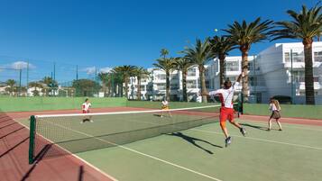 A tennis court with a net, palm trees, and a building in the background.
