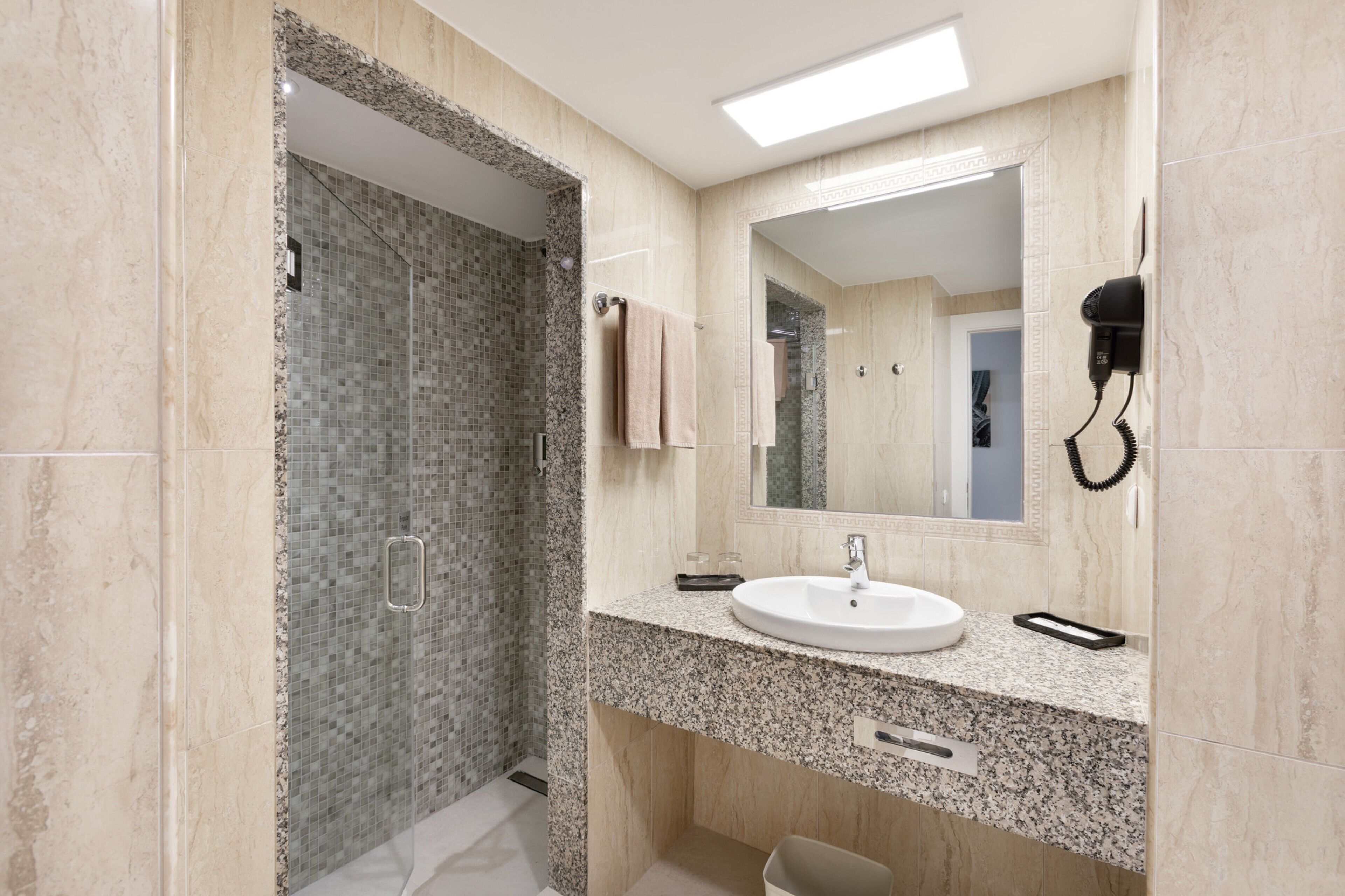 Un baño moderno con encimera de granito, un lavabo, un espejo y un secador de pelo montado en la pared.