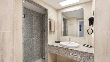 Un baño moderno con encimera de granito, un lavabo, un espejo y un secador de pelo montado en la pared.