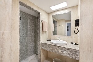 Un baño moderno con encimera de granito, un lavabo, un espejo y un secador de pelo montado en la pared.