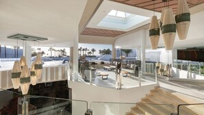 A modern interior with a glass railing, wooden staircase, and hanging pendant lights. - Hotel Riu Paraiso Lanzarote - All Inclusive (Tías)
