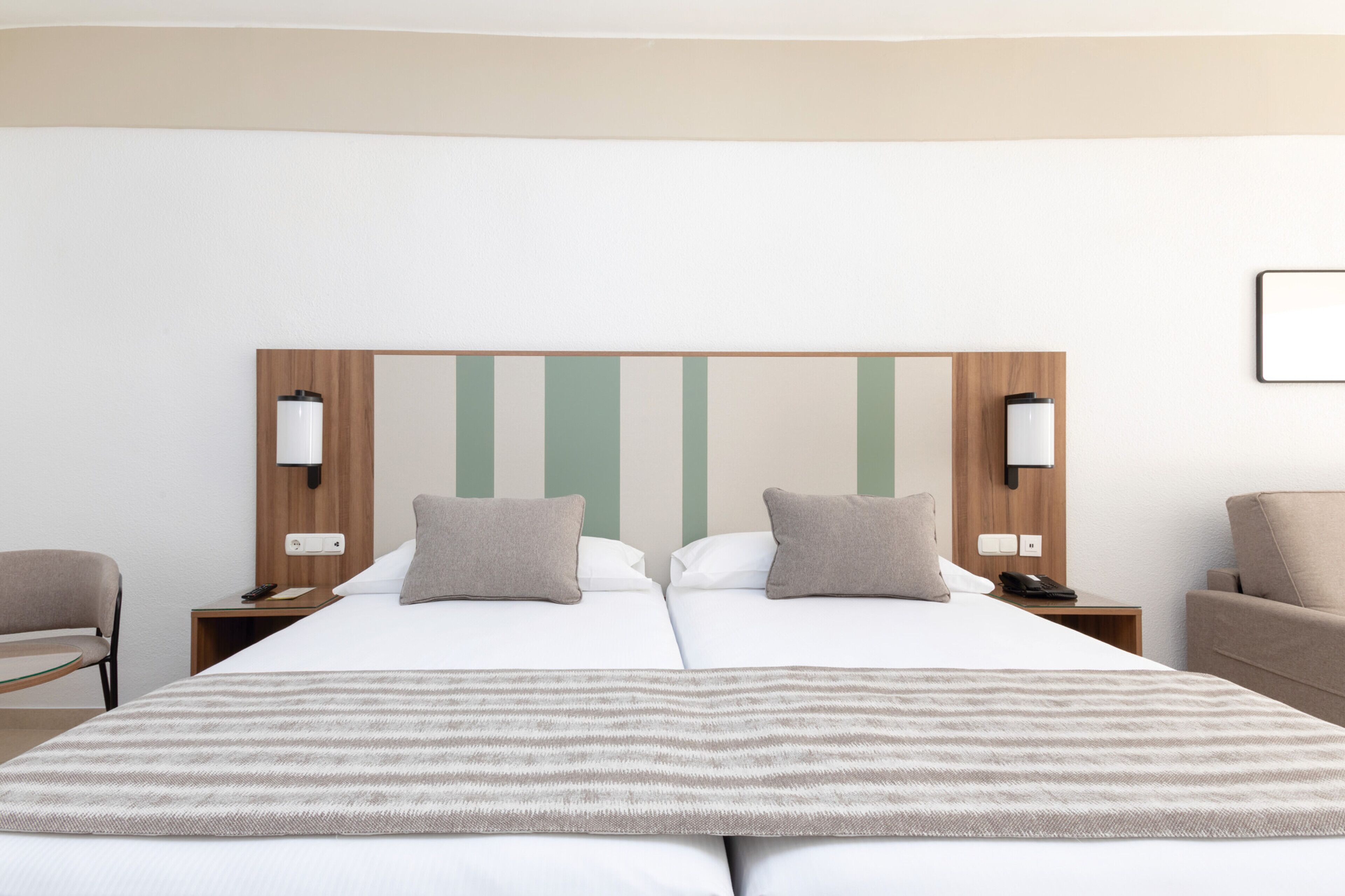 Una cama doble con una manta a rayas, dos mesitas de noche con lámparas, un cabecero de madera y una silla.