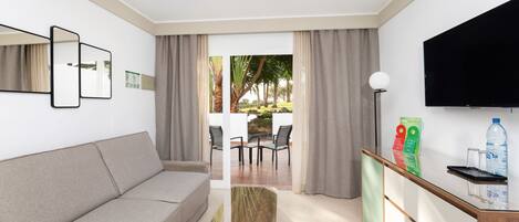 Una sala de estar moderna con un sofá, una mesa de centro de vidrio, un televisor de pantalla plana y vista a un patio exterior con sillas y una mesa.