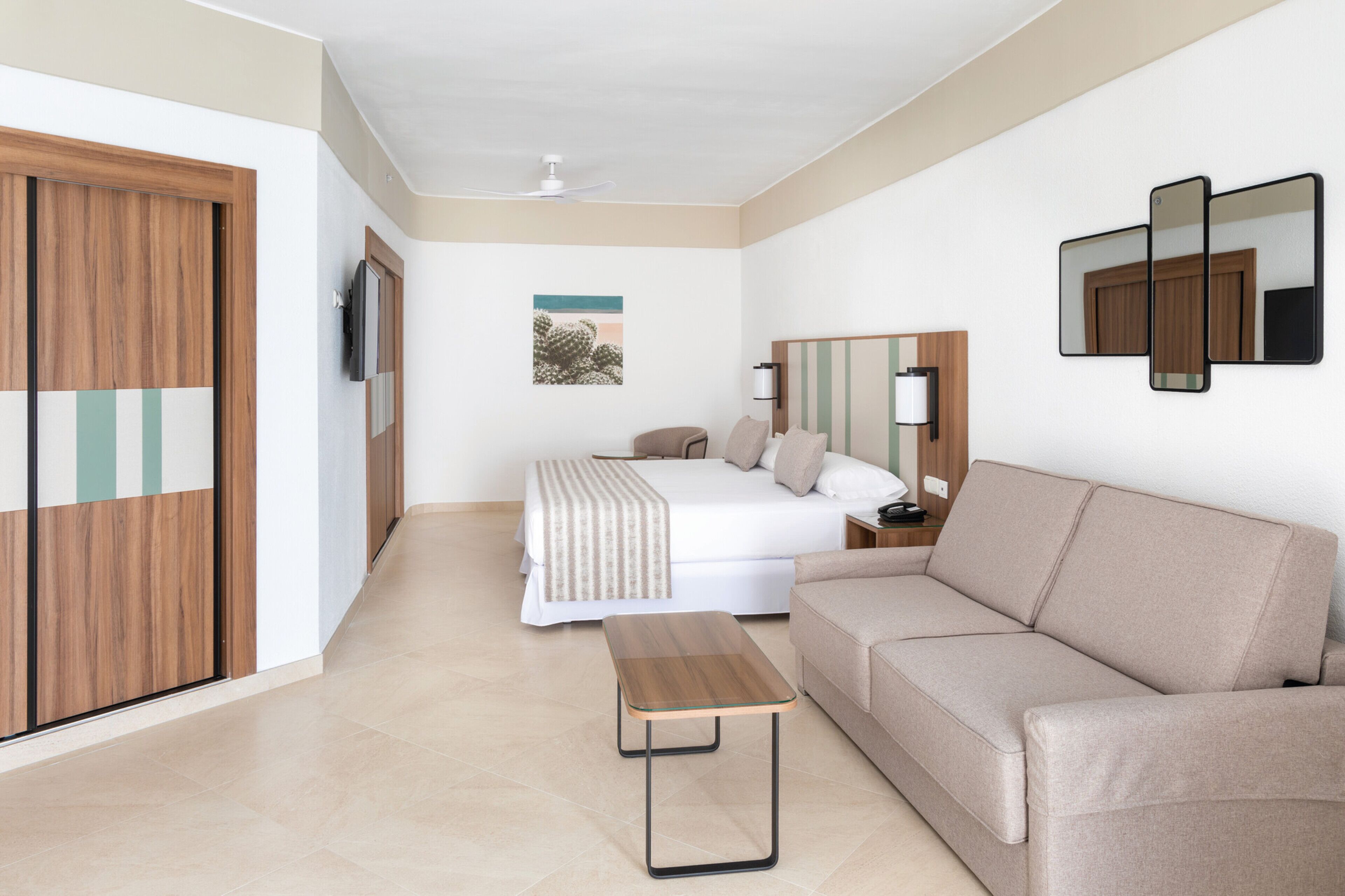 Habitación de hotel con cama, sofá, una mesita, televisor y un cuadro en la pared.