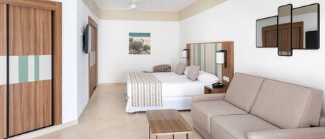 A hotel room with a bed, a sofa, a small table, a TV, and a painting on the wall.