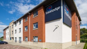 A Travelodge hotel with a modern design, featuring a mix of brick and white exterior, multiple windows, and a clear sky.