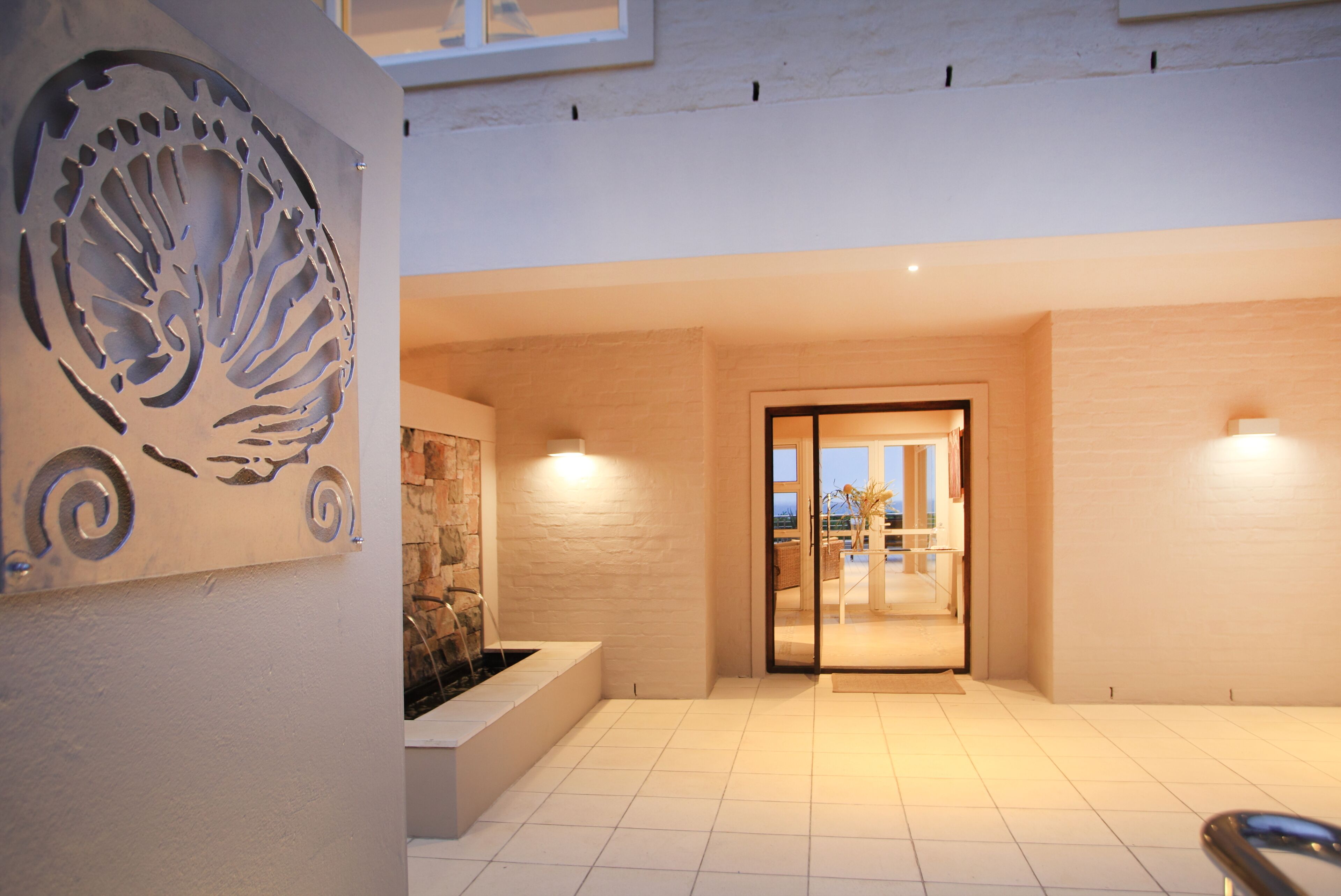 Amplio espacio interior con diseño moderno, que incluye un gran panel decorativo de metal, una zona de estar con un jardín vertical y un ventanal que da a un espacio exterior.