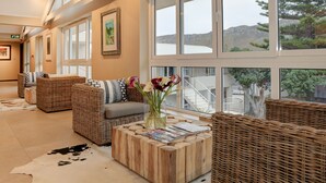 A spacious living area with wicker furniture, a large window with a view of the outdoors, and a cowhide rug. - Abalone Guest Lodge (Hermanus)