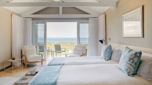 A hotel room with two beds, a balcony with a view of the sea, a ceiling fan, and a table with a tray of items. - Abalone Guest Lodge (Hermanus)