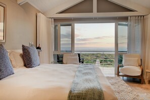 Un dormitorio amplio con una cama grande, vista al mar y un balcón con una silla.