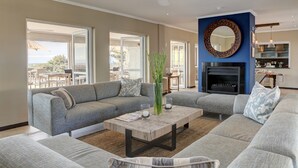 A spacious living room with a grey sectional sofa, a wooden coffee table, and a fireplace. - Abalone Guest Lodge (Hermanus)