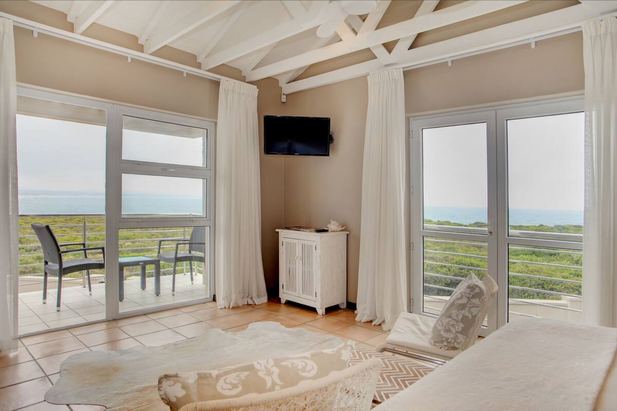 A room with a large sliding glass door leading to a balcony, a white cabinet, a television mounted on the wall, and a patterned rug on the floor.