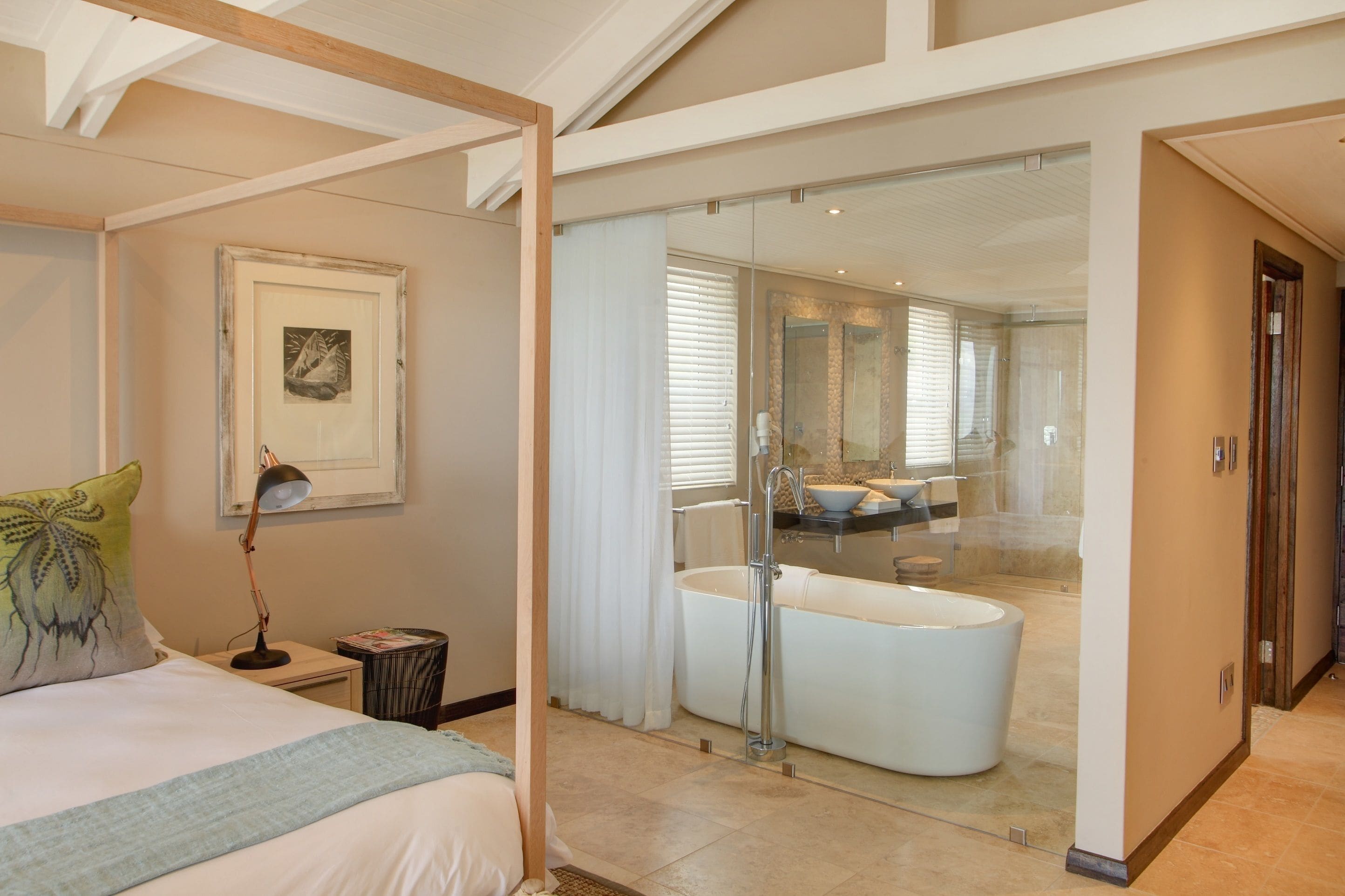 Une chambre moderne avec un grand lit, une lampe de chevet, un tableau encadré et une vue sur une salle de bain équipée d’une baignoire et d’une douche.