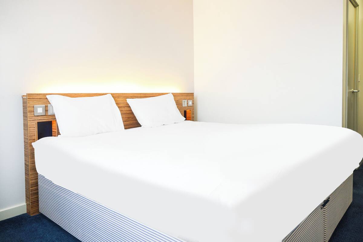 Ein ordentlich gemachtes Bett mit weißen Bettwäsche, einem hölzernen Kopfteil und Nachttischlampen.