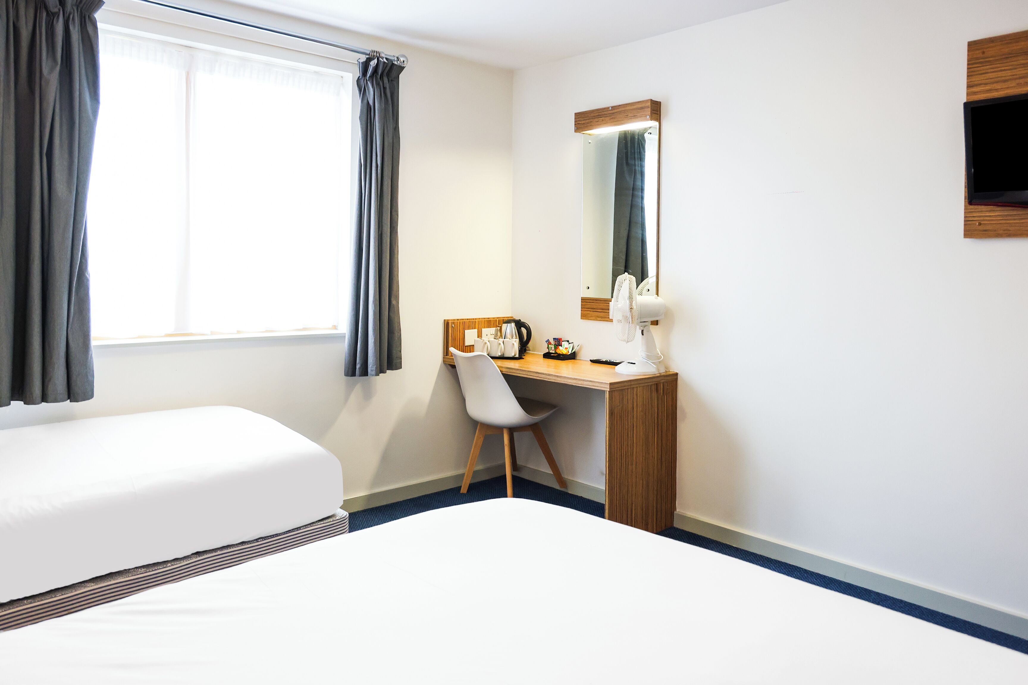 A hotel room with a bed, a desk, a chair, a mirror, and a window with curtains.