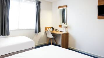 Ett hotellrum med en säng, ett skrivbord, en stol, en spegel och ett fönster med gardiner.