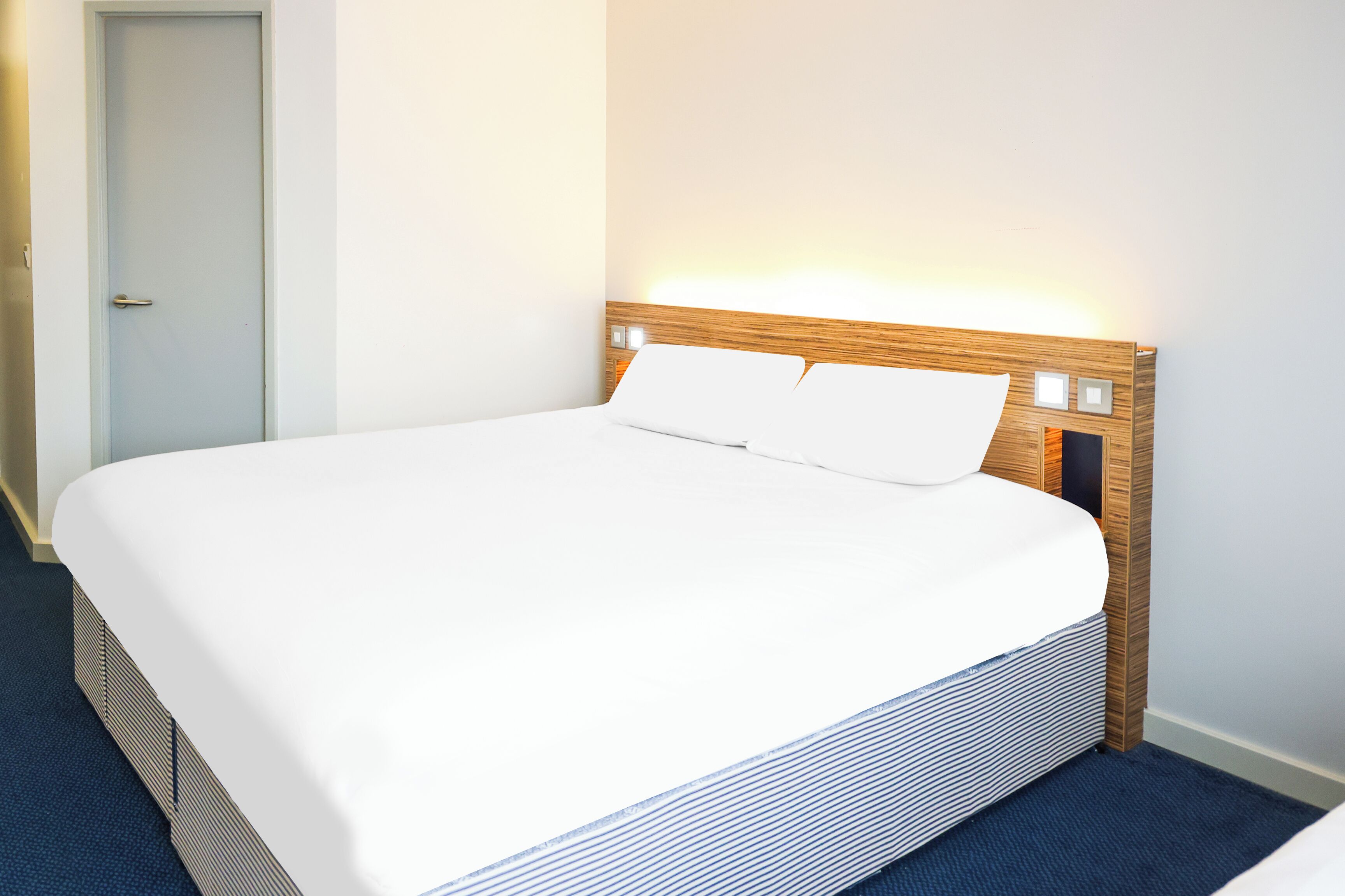A neatly made bed with a wooden headboard and white bedding in a hotel room.