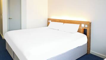 A neatly made bed with a wooden headboard and white bedding in a hotel room.