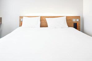 A neatly made bed with a wooden headboard, two white pillows, and a white bedspread. - GO2 Lancaster Centre Hotel by OYO (Lancaster)