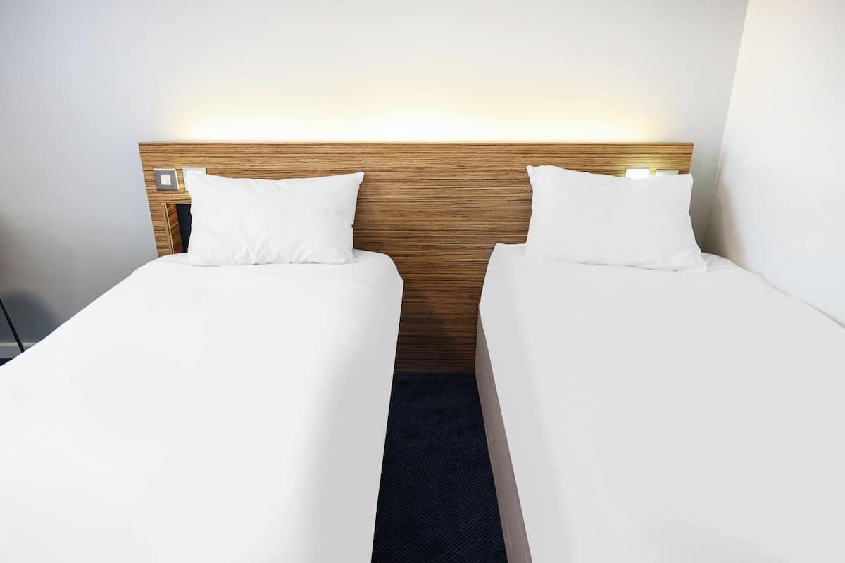 Ein Hotelzimmer mit zwei Einzelbetten, einem Holzkopfstück und einem Nachttisch mit Lampe.