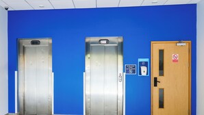 Two elevators and a door with a fire alarm and a "Stay Safe" sign.