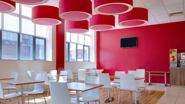 Un espace de restauration moderne avec des chaises et des tables blanches, des murs rouges et de grandes fenêtres.