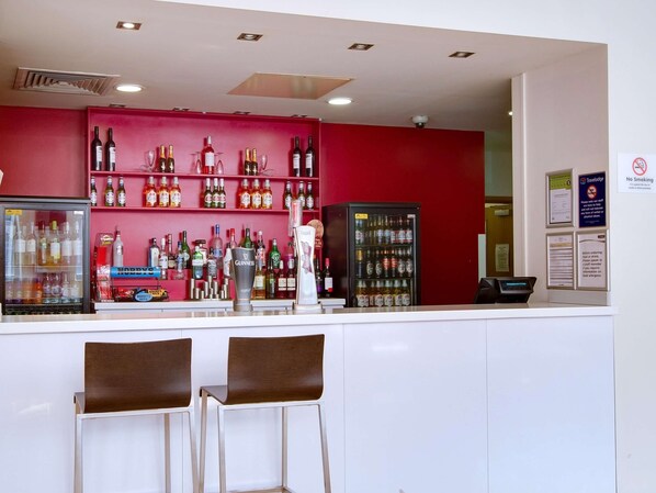 Un espace bar avec des étagères remplies de bouteilles d’alcool, un réfrigérateur et un distributeur automatique.