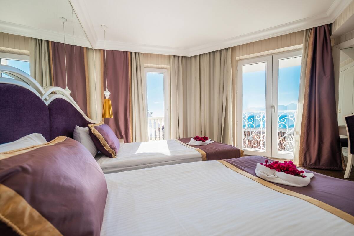 A hotel room with two beds, a balcony with a railing, and a view of the sky.