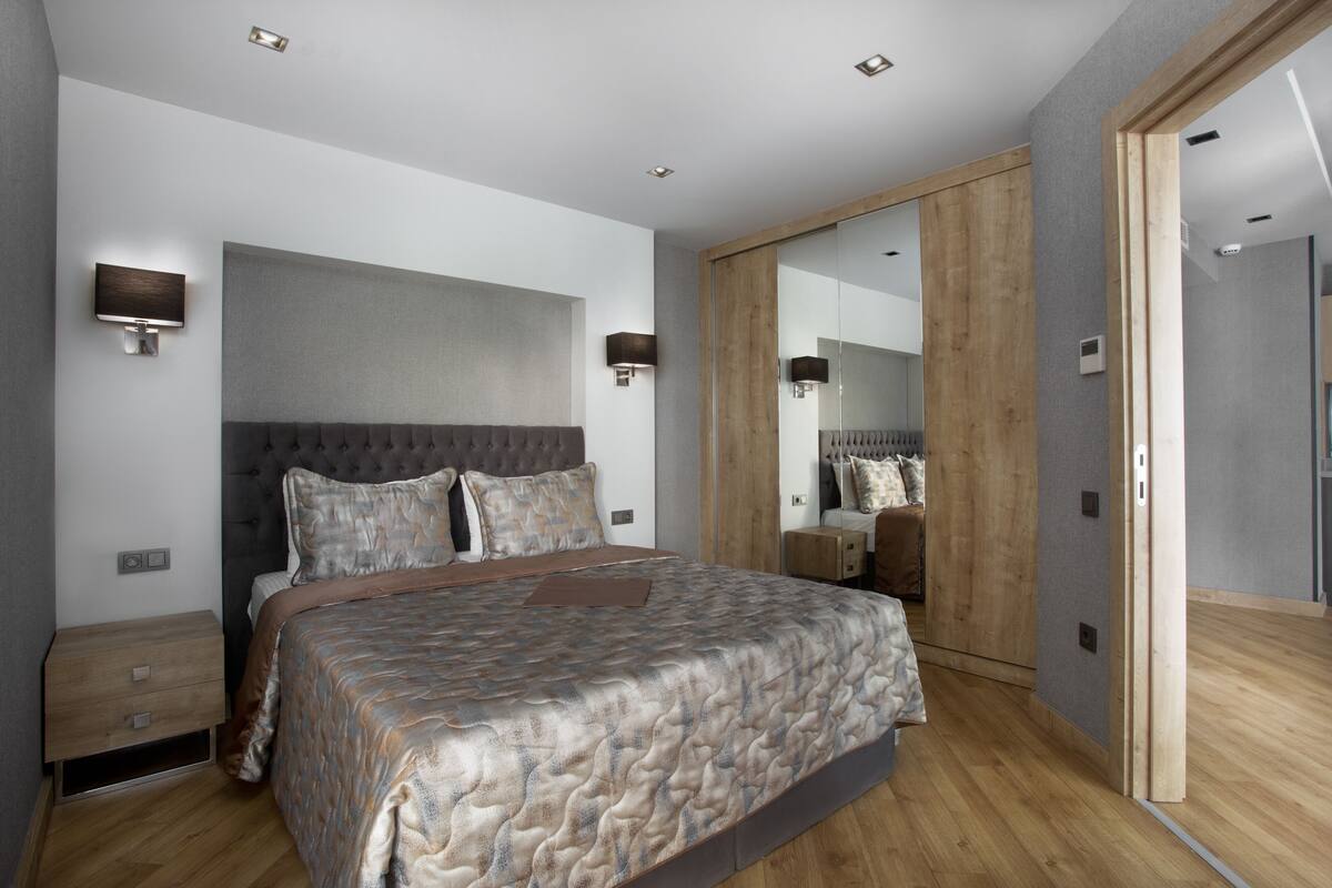 A modern bedroom with a large bed, bedside tables, a wardrobe, and a mirror.