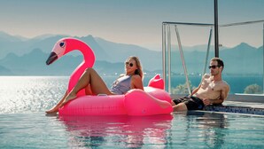 A pool with a view of mountains, a pink flamingo float, and two people relaxing.