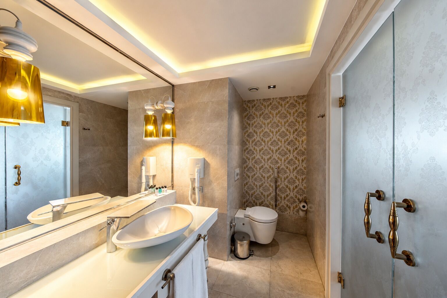 Et moderne badeværelse med et stort spejl, en vask, et toilet og et bruseområde.