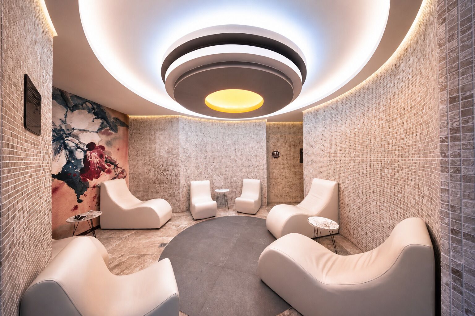 A spa room with a circular seating area, a mural on the wall, and a unique ceiling design.