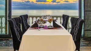 A dining table set for two with a view of the sea and sunset.