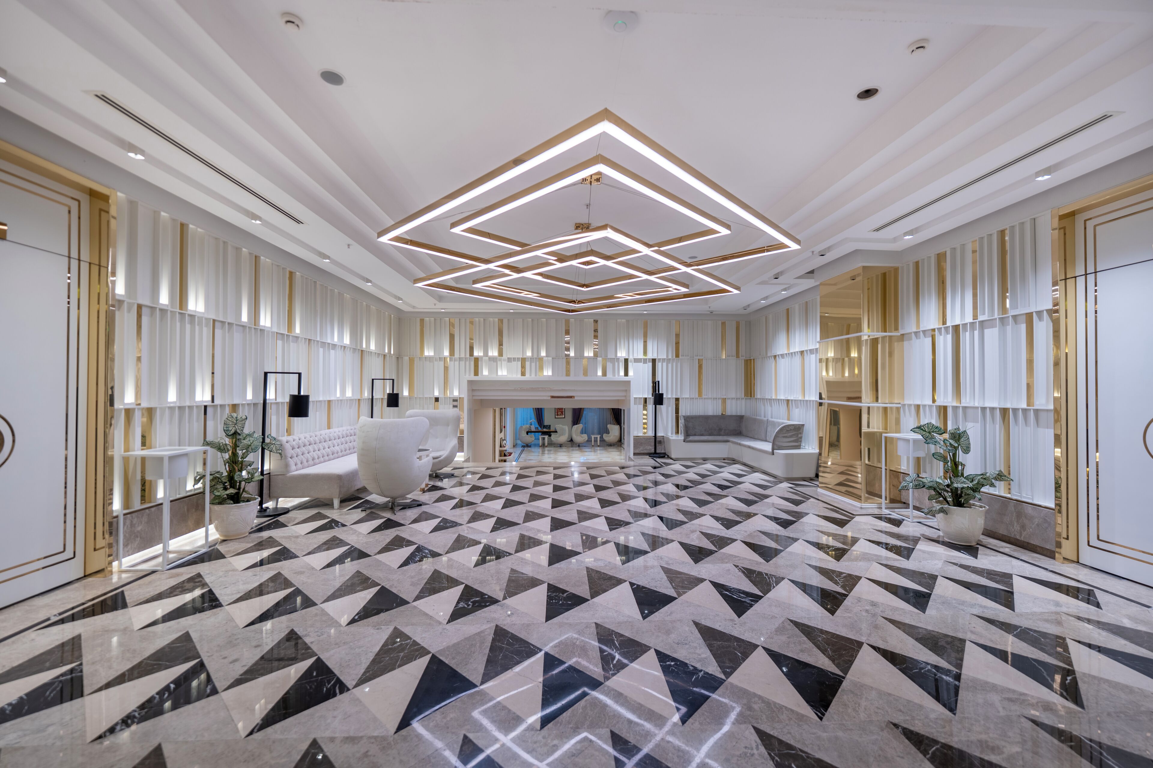 Un hall espacioso con suelo de diseño geométrico, un área de descanso central y un techo de estilo moderno.
