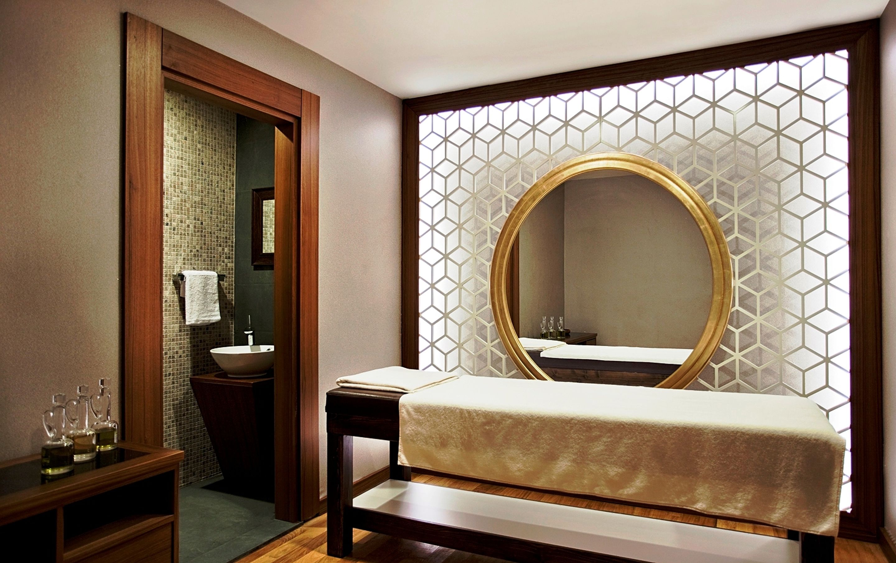 A hotel room with a wooden bed, a bedside table with a mirror, a sink, and a decorative wall with a geometric pattern.