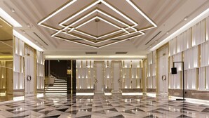A spacious lobby with a geometric ceiling design, a checkered floor, and a symmetrical layout with doors on either side.