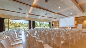 A conference room with rows of white chairs, a projector screen, and a large window offering a view of trees and a building. - Best Western Plus Leone di Messapia Hotel & Conference (Lecce)