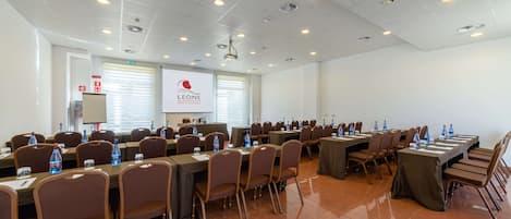 A conference room with multiple tables and chairs, equipped with water bottles and projectors.