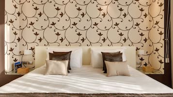 Una cama bien hecha con sábanas blancas y almohadas con estampado floral marrón, una mesita de noche con lámpara y una pared con papel tapiz decorativo con motivos florales.
