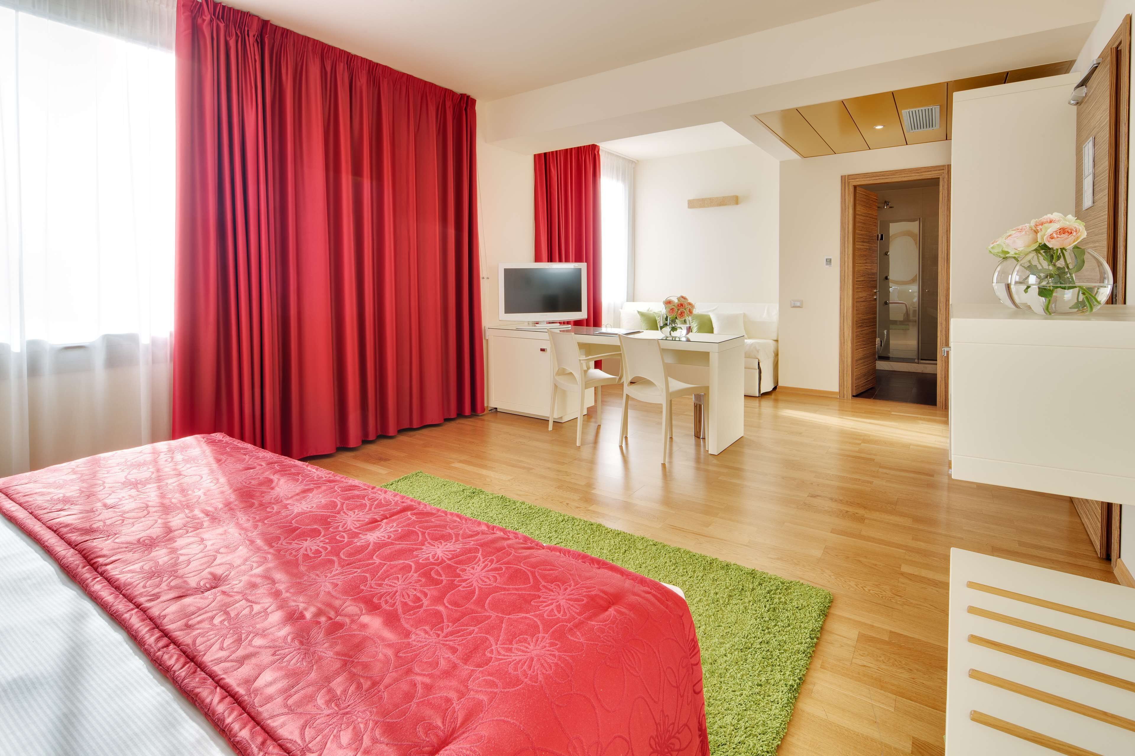 Quarto de hotel com cama, escrivaninha, televisão e banheiro visível através de uma porta aberta.