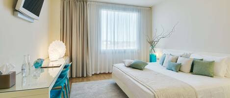 Habitación de hotel con cama, escritorio, silla, televisor y ventana con cortinas.