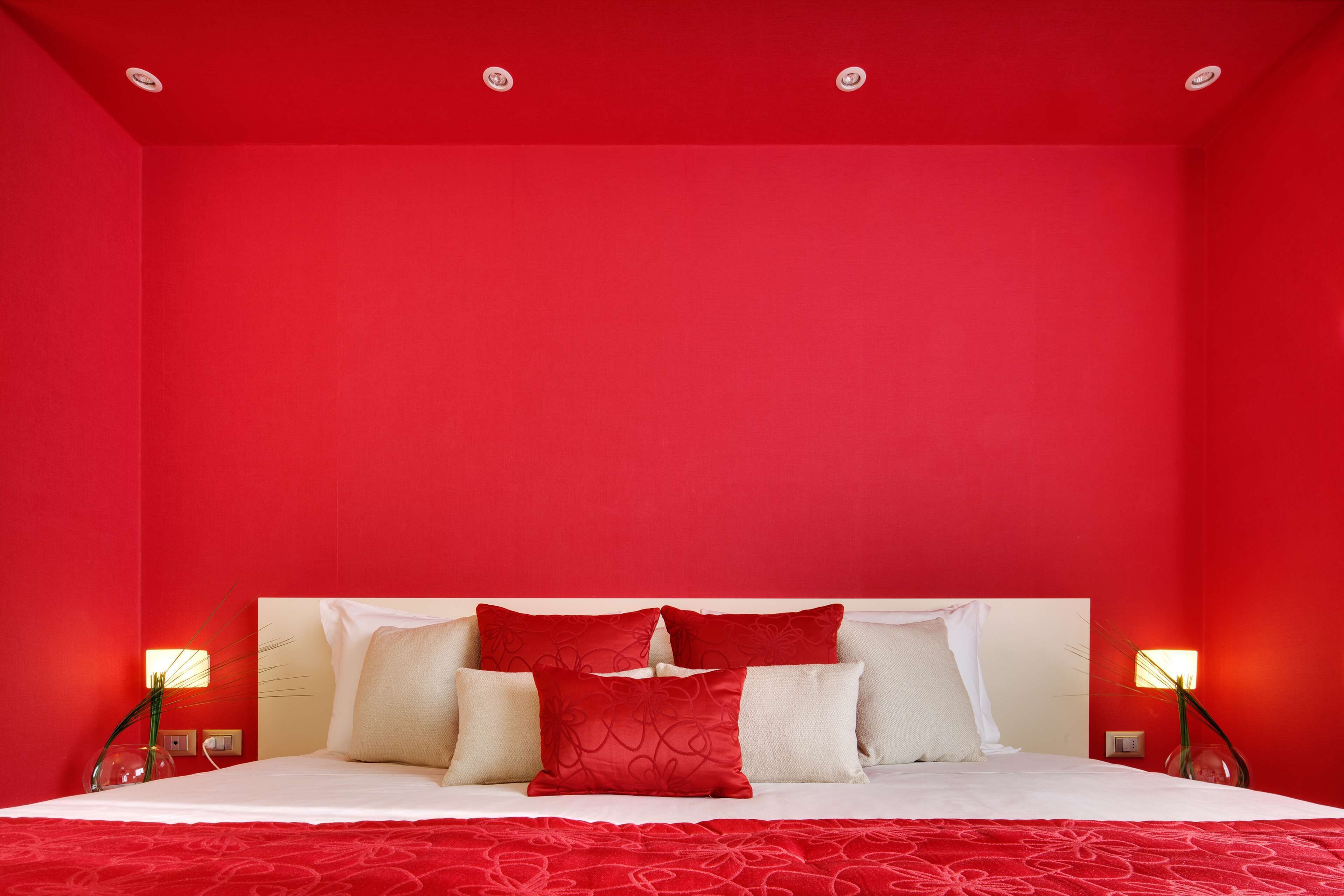 Une chambre d’hôtel avec un mur rouge, un lit blanc avec des oreillers rouges et blancs, et deux lampes de chevet.