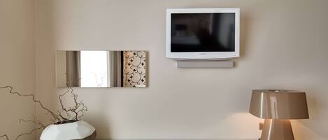 Una habitación moderna con televisor de pantalla plana, un florero decorativo, una lámpara y una mesa de vidrio.