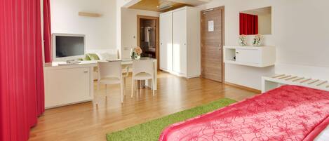A modern hotel room with a bed, desk, chairs, and a TV.