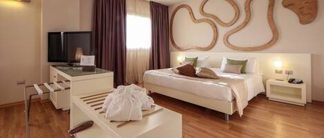 A modern hotel room with a bed, a desk with a flat-screen TV, a bedside table, and a large abstract wall decoration.