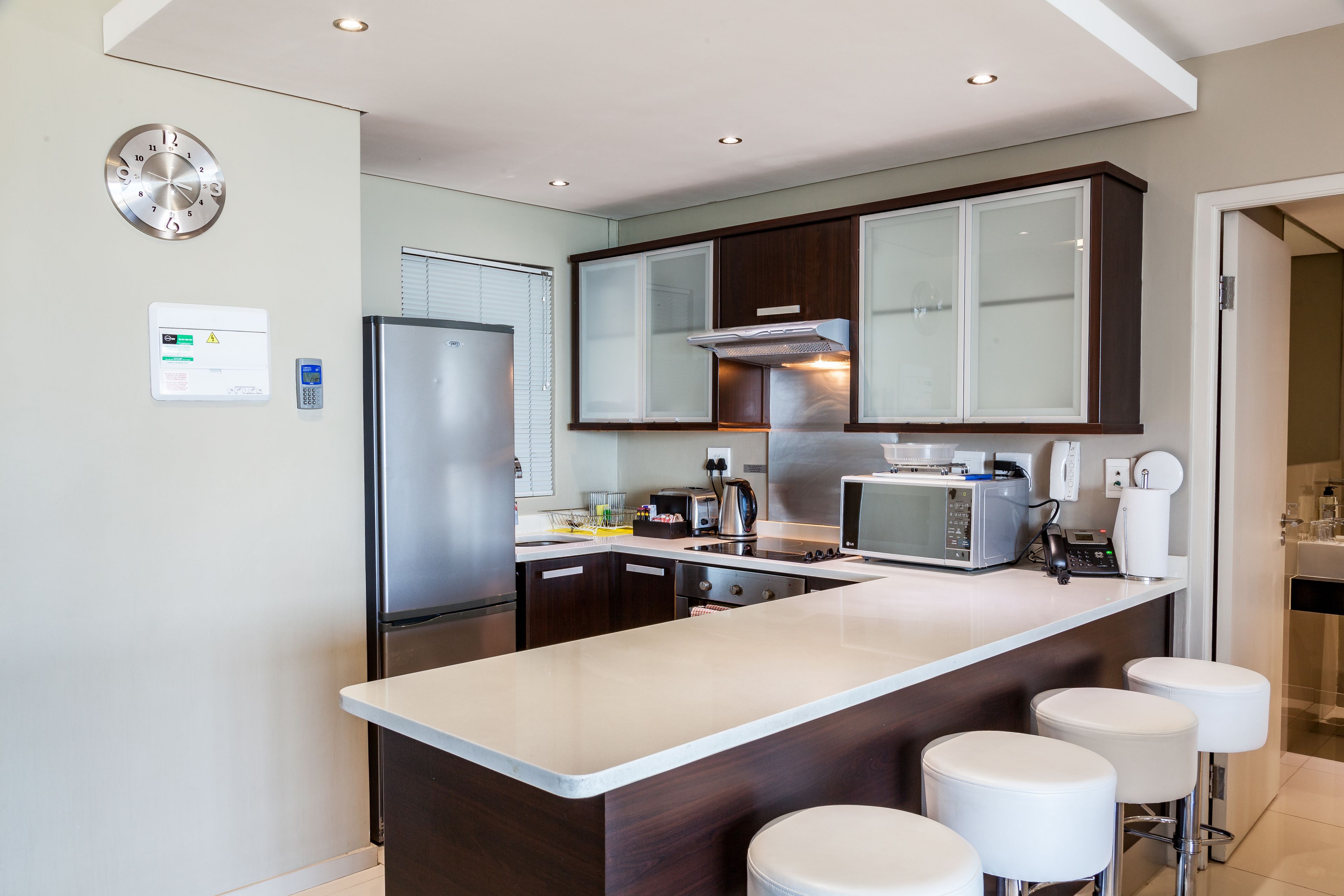A modern kitchen with a central island, bar stools, a built-in microwave, and a stainless steel refrigerator.