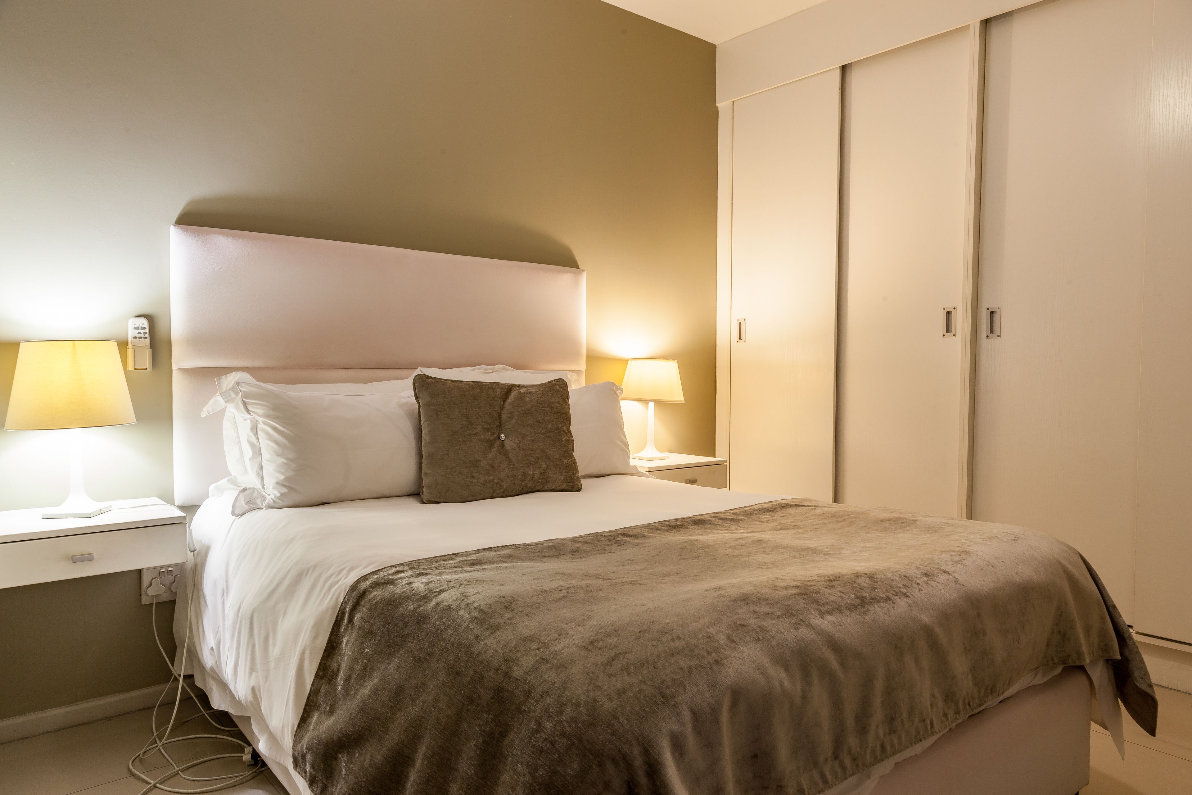 A neatly made bed with white and brown bedding, two bedside lamps, and a wardrobe with a sliding door.
