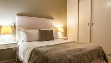 A neatly made bed with white and brown bedding, two bedside lamps, and a wardrobe with a sliding door.