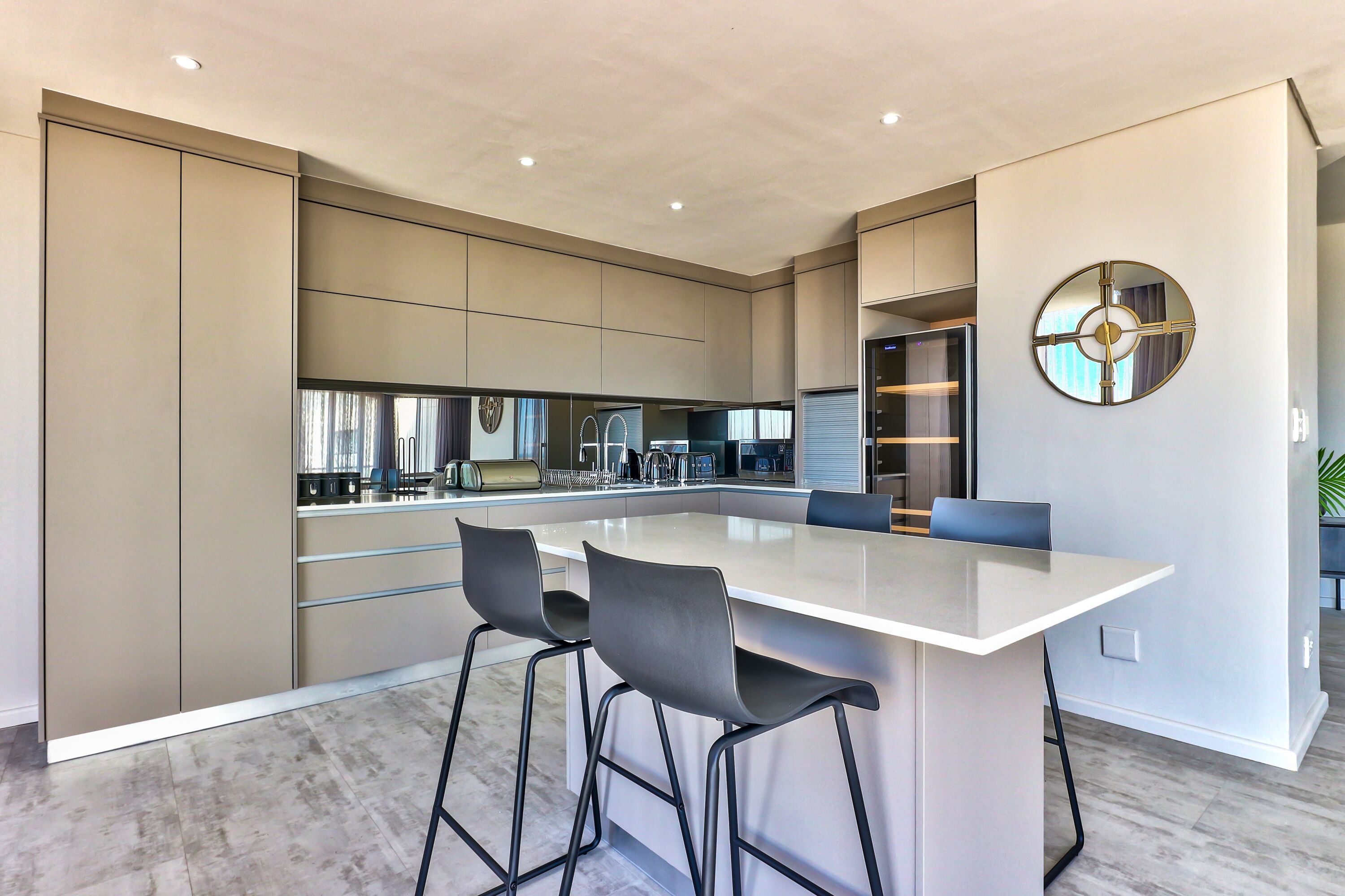 Een moderne keuken met een groot kookeiland, barstoelen en een decoratieve spiegel.